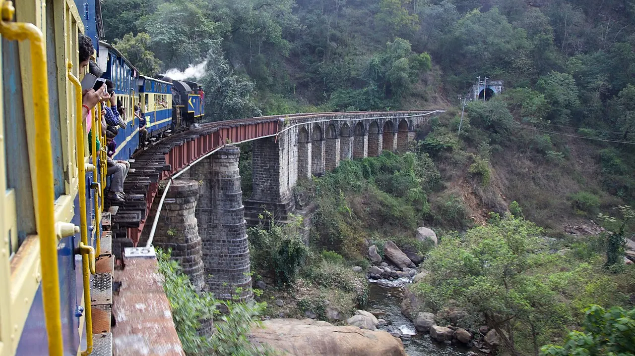 Nilgiri Mountain Railway train crossing a stone arch bridge over a river